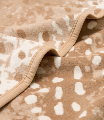 Beige knit blanket with white deer spot pattern and bound edges.5