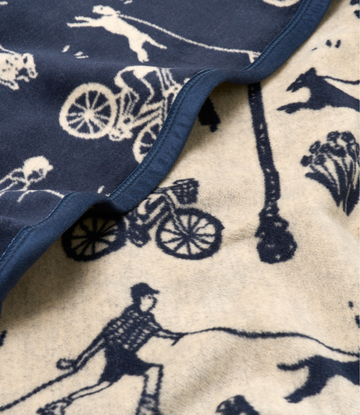 Navy and cream blanket with dogs, bicycles, and people playing pattern, navy binding on edges.5