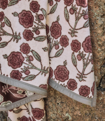 Cream blanket with burgundy and green blockprint raspberry and leaf pattern, folded on textured ground.4