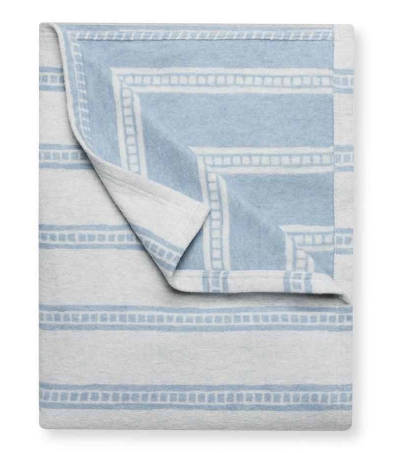 Light blue and white blanket with geometric tile stripe pattern, partially folded to show reverse side.