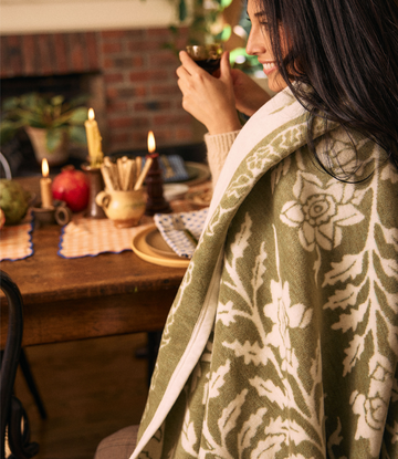 Woman wearing sage green blanket with cream tree and leaf pattern draped over shoulders at dining table.4
