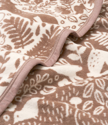 Tan and cream blanket with woodland animal and foliage jacquard pattern, finished with mauve binding.5