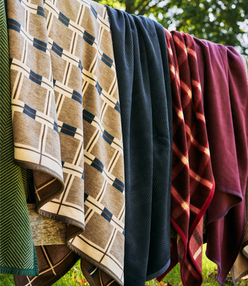 Tan grid blanket with navy squares hanging on clothesline with other colorful blankets outdoors.4