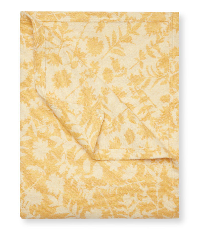 Yellow and cream floral patterned lightweight blanket with daffodil and leaf designs folded on itself.